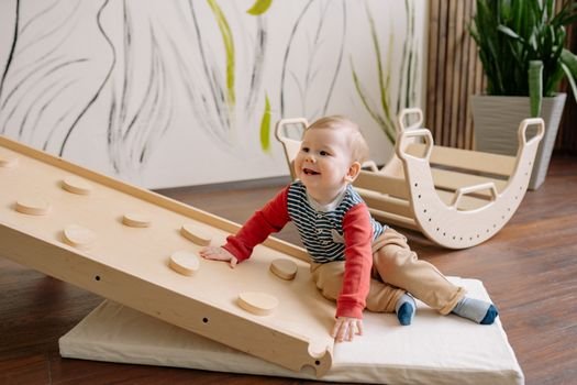 Cheerful toddler playing on a wooden climbing ramp indoors, smiling happily.