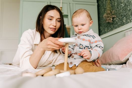 A mother and baby play together on a bed with wooden toys, fostering closeness and learning.