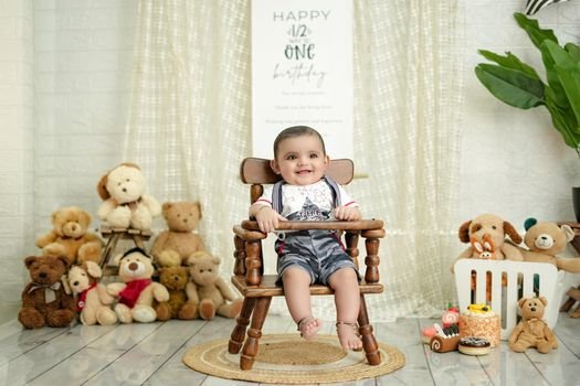 A baby celebrates half birthday indoors with teddy bears, cake, and decorations.