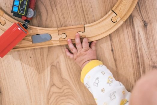 A toddler's hand assembling a wooden toy train track on a hardwood floor.