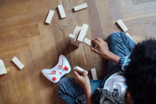 Child playing with wooden blocks and a toy controller on a wooden floor indoors.