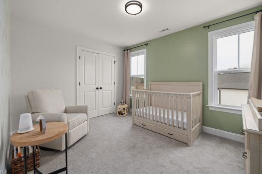 A serene modern nursery with a crib, armchair, and green accent wall.