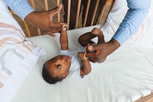 A tender moment showing a father lovingly holding his baby's hand while the baby lies in a crib.