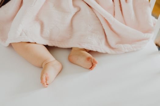 Adorable newborn baby feet peeking from under a soft, pink blanket on a white bed.