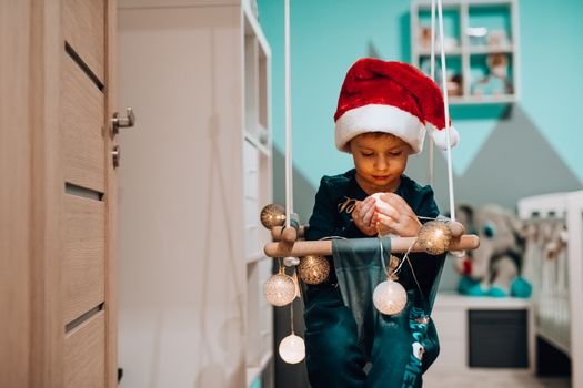 A child in a Santa hat sitting on a swing indoors, embracing Christmas decor.