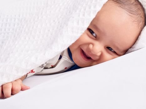 Adorable baby smiling under a white blanket. Captivating expression and innocent joy.