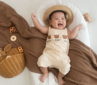 Cheerful baby wearing a cute outfit and sun hat lying on cozy bedding.