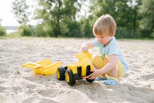 A young boy enjoys playing with a yellow toy truck on a sandy outdoor area. Perfect for playtime imagery.