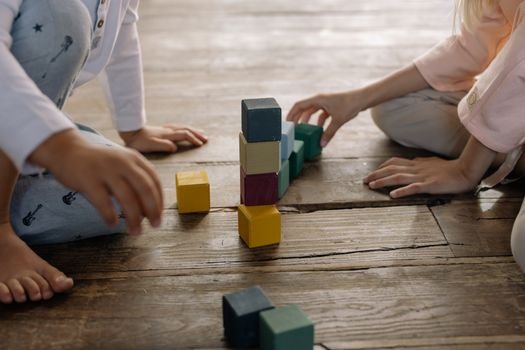 Kids engaged in building with multicolored wooden blocks on a wooden floor.