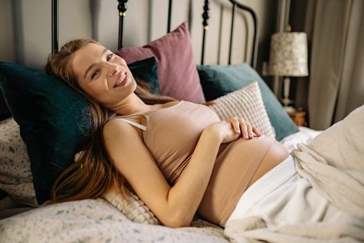 Pregnant woman feeling cozy and relaxed, lying on a comfortable bed at home.