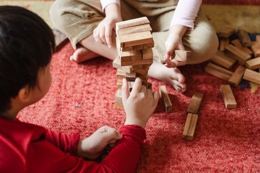 Two children enjoying a game of Jenga on a cozy carpet, emphasizing playtime and interaction.